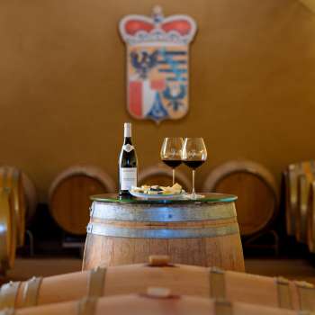 Weinfasskeller mit Flasche Rotwein und zwei Gläsern vor dem Wappen der Hofkellerei in Liechtenstein