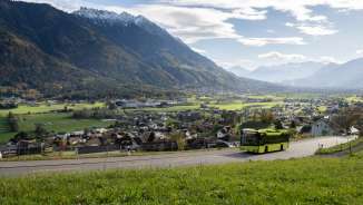 Grüner LIEmobil Bus fährt eine kurvige Straße oberhalb von Liechtenstein entlang mit Blick auf das Rheintal und die umliegenden Alpen