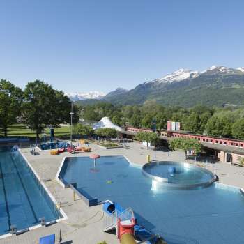 Gesamtansicht des Freibads Mühleholz mit mehreren Becken und herrlichem Alpenpanorama im Hintergrund.