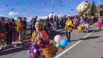 Fasnachtsumzug mit bunten Kostümen in Triesenberg Clown verkleidet mit Konfetti und Luftballons beim Fasnachtsumzug, Zuschauende am Strassenrand.