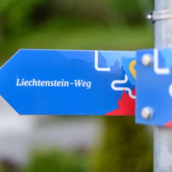 Blauer Wegweiser mit Aufschrift „Liechtenstein-Weg“ in moderner Gestaltung.