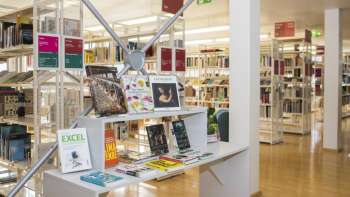 Heller Eingangsbereich der Liechtensteinischen Landesbibliothek mit modernen Bücherregalen und Ausstellungsfläche für Neuerscheinungen