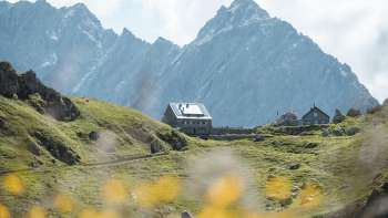Pfälzerhütte mit Bergkulisse im Hintergrund und Blumen im Vordergrund.