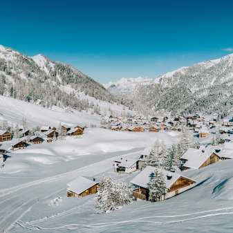 Luftaufnahme von Malbun im Winter mit verschneiten Holzhäusern, eingebettet in die Alpenlandschaft Liechtensteins