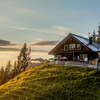 Gafadurahütte auf grüner Anhöhe in Liechtenstein bei Sonnenuntergang mit Panoramablick über die Berge