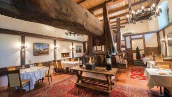 Rustikaler Speisesaal mit historischem Holzbalken, Kamin und gedeckten Tischen im Restaurant Torkel.