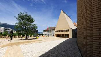 Blick auf den hell gepflasterten Peter-Kaiser-Platz vor dem Landtagsgebäude in Vaduz mit modernem Architekturensemble.