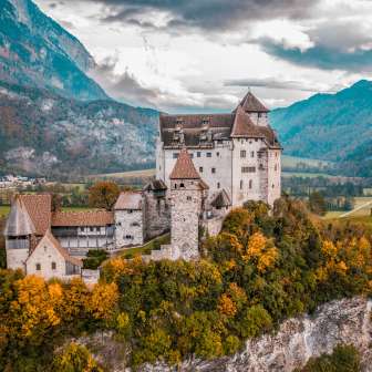 Panoramaaufnahme der mittelalterlichen Burg Gutenberg in Liechtenstein mit bunter Herbstlandschaft und Alpenkulisse