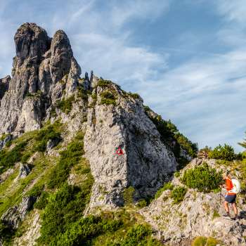 Wanderer auf felsigem Bergpfad vor zerklüftetem Grat mit rot-weissem Wegzeichen