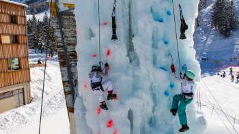 Zwei Kinder beim Eisklettern am gefrorenen Kletterturm in Malbun mit Eispickeln und Helmen