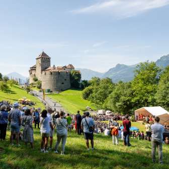 Besucher versammeln sich zum Staatsakt 2024 in Liechtenstein auf der Wiese unterhalb von Schloss Vaduz