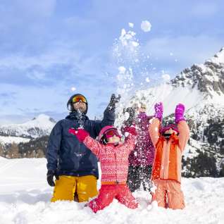 Familie geniesst gemeinsam den Schnee in Malbun – Kinder werfen fröhlich Schneebälle vor winterlicher Bergkulisse.