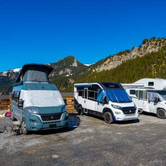 Mehrere Camper und Wohnmobile auf einem Stellplatz in den Bergen von Liechtenstein bei strahlend blauem Himmel