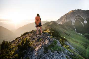 Frau mit Rucksack genießt den Sonnenaufgang beim Wandern in Malbun mit Blick auf die Berglandschaft