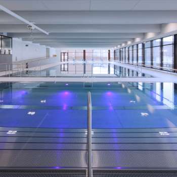 Modernes Hallenbad in Triesen mit beleuchtetem Schwimmbecken und großzügiger Glasfront.