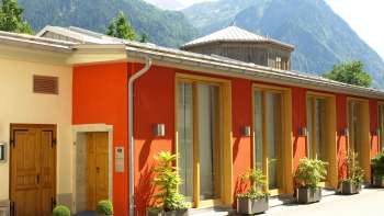 Außenansicht des Gasometer Kulturzentrums mit farbenfroher Fassade und Alpenpanorama im Hintergrund.