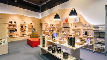Helles Besucherzentrum mit modernen Holzregalen, gefüllt mit Souvenirs, Spezialitäten und Informationsmaterialien. Helles Besucherzentrum mit modernen Holzregalen, gefüllt mit Souvenirs, Spezialitäten und Informationsmaterialien.