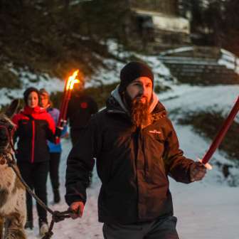 Gruppe bei einer geführten Lamawanderung im verschneiten Liechtenstein mit Fackeln – stimmungsvolles Outdoor-Abenteuer für Groß und Klein.