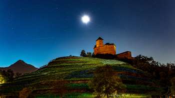 Die beleuchtete Burg Gutenberg bei Nacht unter Vollmond, eingebettet in die Weinberge