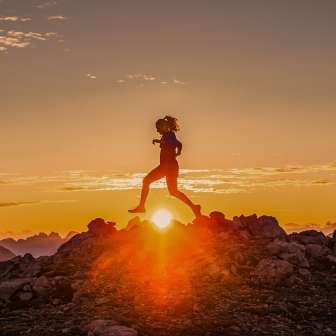 Zwei Trailrunner überqueren einen felsigen Bergrücken bei Sonnenaufgang in Liechtenstein, im goldenen Licht der Morgendämmerung