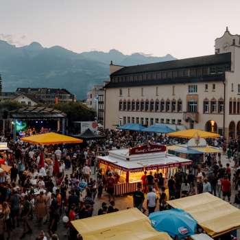 Das Rathaus Vaduz bei Dämmerung mit Lichterketten, spielenden Kindern auf einem Tischtennistisch und sommerlicher Atmosphäre am Staatsfeiertag