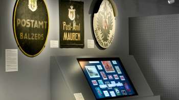 Museumsraum mit alten Postschildern und einem digitalen Display zur Geschichte der Post in Liechtenstein.
