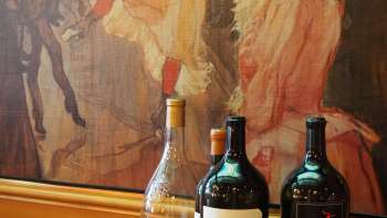 Drei Weinflaschen vor einem kunstvollen Wandgemälde in der Brasserie Burg – mediterrane Eleganz trifft Kunstflair.