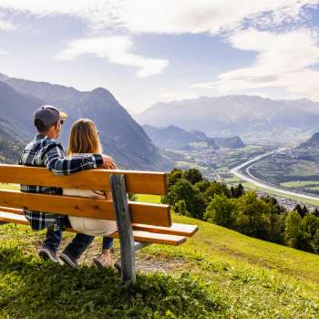 Paar auf einer Holzbank mit Aussicht auf das Rheintal und die Berge.