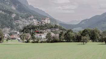 Majestätische Aussicht auf Burg Gutenberg in Balzers, umgeben von grünen Feldern und den beeindruckenden Alpen.