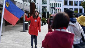Stadtführerin mit Liechtenstein-Fahne begrüßt Touristengruppe in Vaduz bei der City-Classic Tour Stadtführerin mit Liechtenstein-Fahne begrüßt Touristengruppe in Vaduz bei der City-Classic Tour