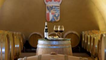 Stimmungsvolle Weinprobe im Weinkeller des Fürstlichen Weinguts mit zwei Gläsern und einer Flasche Rotwein auf einem Holzfass.