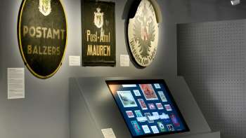 Museumsraum mit alten Postschildern und einem digitalen Display zur Geschichte der Post in Liechtenstein.