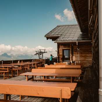 Leere Holzbänke auf der Aussichtsterrasse der Sareis-Hütte mit Blick auf die Alpen – ideal für eine Rast während einer Wanderung oder Fahrt mit der Bergbahn.