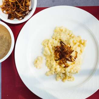 Traditionelle Käsknöpfle mit Röstzwiebeln und Apfelmus aus Liechtenstein auf weißem Teller