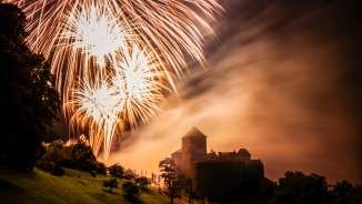 Schloss Vaduz in Liechtenstein bei Nacht mit großem Feuerwerk am Himmel – stimmungsvolle Aufnahme mit Licht und Nebel
