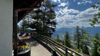 „Sonnenterrasse mit Panoramablick über das Rheintal bei klarer Sicht und gemütlicher Sitzgelegenheit im Alpenstil im Berggasthaus Matu