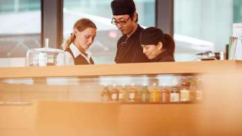 Drei Mitarbeitende des Cafés im Kunstmuseum, die gemeinsam an der Theke arbeiten und sich konzentriert austauschen.