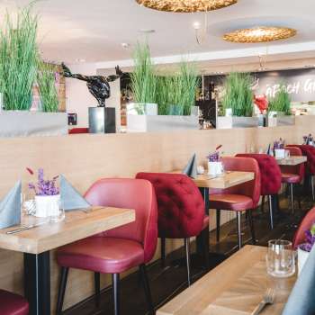 : Großzügig gedeckte Tische im PUR Restaurant & Bar mit roten Stühlen und floraler Tischdekoration.