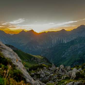 Sonnenuntergang am Grat – Die Sonne versinkt hinter den Bergspitzen und taucht das alpine Panorama in warme Abendfarben