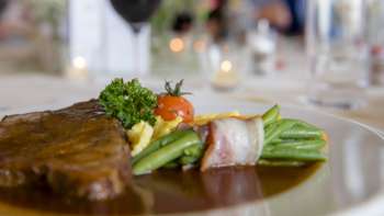 Detailaufnahme eines Hauptgerichts mit grünem Gemüse, Speck und cremiger Sauce auf dem Teller