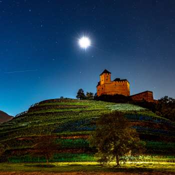 Die beleuchtete Burg Gutenberg bei Nacht unter Vollmond, eingebettet in die Weinberge.
