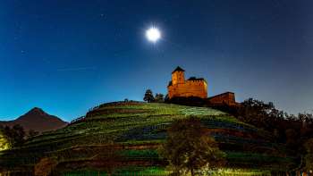 Die beleuchtete Burg Gutenberg bei Nacht unter Vollmond, eingebettet in die Weinberge