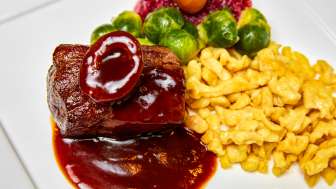Traditionelles Wildgericht mit Spätzle und Rosenkohl Leckeres Wildgericht mit dunkler Sauce, goldgelben Spätzle, Rosenkohl und Preiselbeeren auf einem weissen Teller angerichtet.