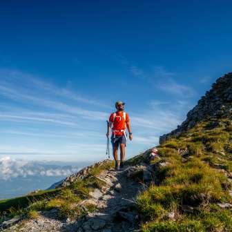 Wanderer mit rotem Shirt auf dem Berggrat der Drei Schwestern entlang der Route 66 mit Blick über die Alpenlandschaft in Liechtenstein