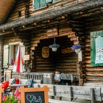 Eingangsbereich der Hütte: Rustikaler Eingangsbereich der Gafadurahütte mit Holzfassade, bunten Blumen und Hinweistafel.