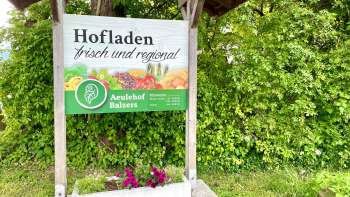 Schild des Hofladens Aeulehof mit Aufschrift „Frisch und regional“ vor grüner Hecke in Triesen.