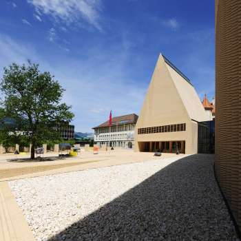 Blick auf den hell gepflasterten Peter-Kaiser-Platz vor dem Landtagsgebäude in Vaduz mit modernem Architekturensemble.