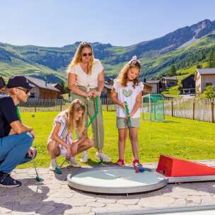 Familie spielt gemeinsam Minigolf im sonnigen Bergdorf Malbun in Liechtenstein – Spaß für Groß und Klein in den Alpen.