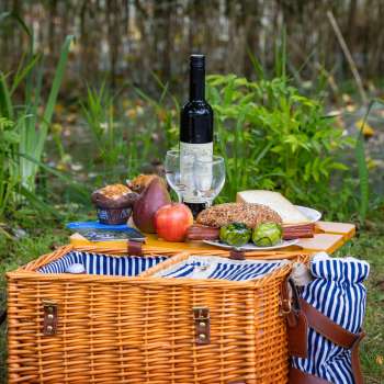 Picknickkorb mit regionalen Spezialitäten, frischem Brot, Obst und Wein, liebevoll angerichtet auf einer Wiese inmitten der Natur.