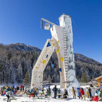 Der vereiste Kletterturm in Malbun umgeben von Wintergästen vor alpiner Kulisse – Highlight für Wintersportbegeisterte in Liechtenstein.